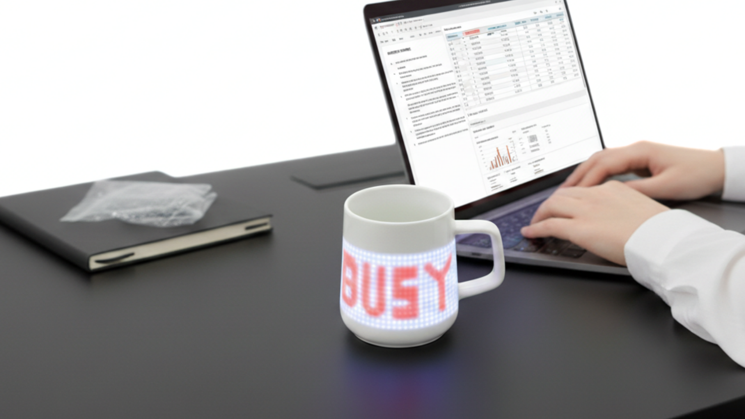 PixelMug displaying BUSY in pixel text on office desk beside laptop, showing do-not-disturb status use case